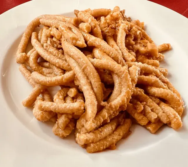 Pici all'aglione, uno dei piatti tipici di Arezzo, serviti su un piatto bianco.